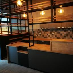 AB Transport - Nowoczesna aranżacja wnętrza lokalu gastronomicznego z drewnianym barem, metalową konstrukcją regałów podwieszanych i dekoracyjną mozaiką na ścianie.