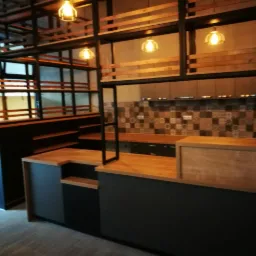 Nowoczesna aranżacja wnętrza lokalu gastronomicznego z drewnianym barem, metalową konstrukcją regałów podwieszanych i dekoracyjną mozaiką na ścianie.