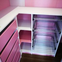 AB Transport - Różowo-biała zabudowa narożna z szufladami i metalowymi koszami cargo, widoczne brązowe panele podłogowe.