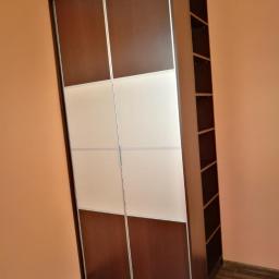 AB Transport - Dwudrzwiowa szafa przesuwna z brązowymi i białymi panelami, z otwartym regałem po prawej stronie, na tle pomarańczowej ściany i drewnianej podłogi.