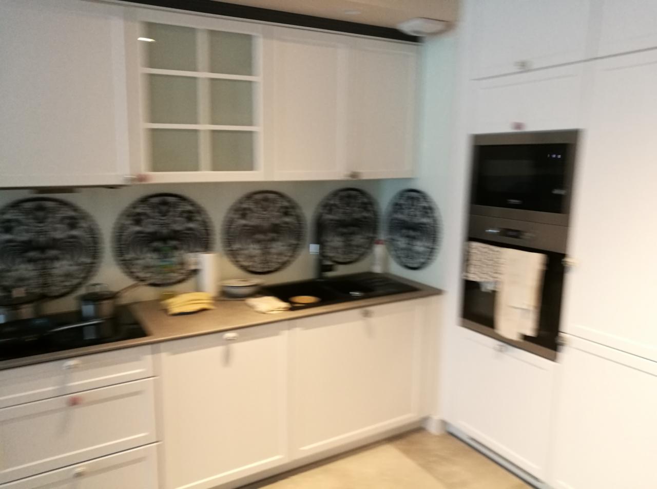 Biała kuchnia z zabudowanymi szafkami, czarnym zlewozmywakiem i wzorzystą dekoracją ścienną w formie okręgów, z wbudowanym piekarnikiem i kuchenką.