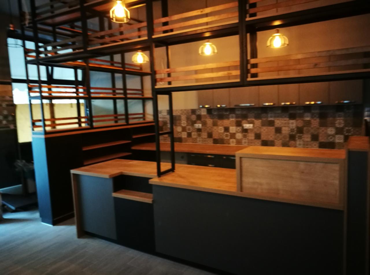 Nowoczesna aranżacja wnętrza lokalu gastronomicznego z drewnianym barem, metalową konstrukcją regałów podwieszanych i dekoracyjną mozaiką na ścianie.
