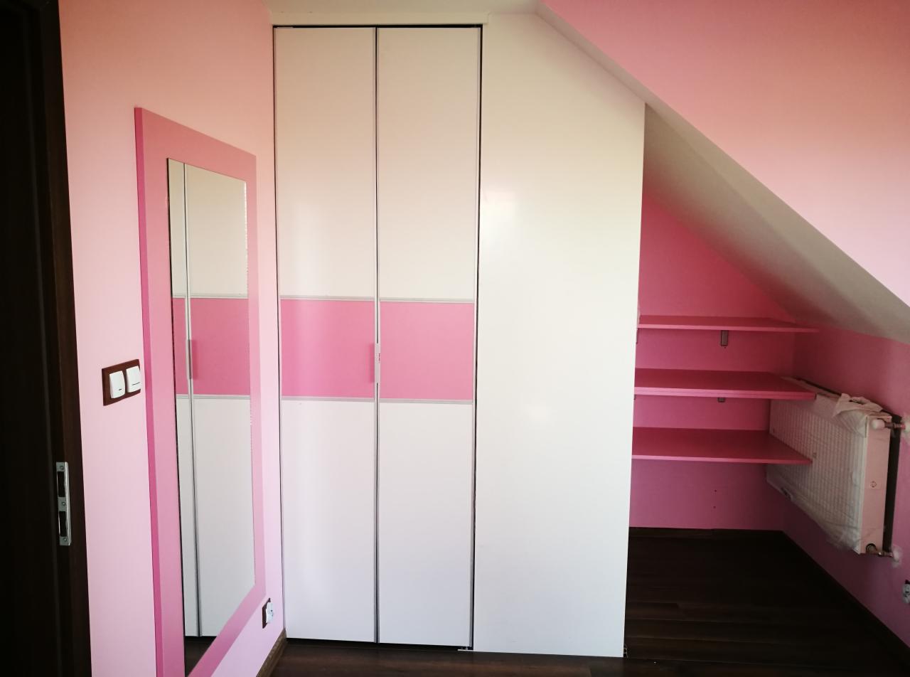 Biała szafa przesuwna z różowym pasem na środku, dopasowana do różowych ścian pokoju na poddaszu, obok lustro w różowej ramie i widoczne półki w skosie dachu.