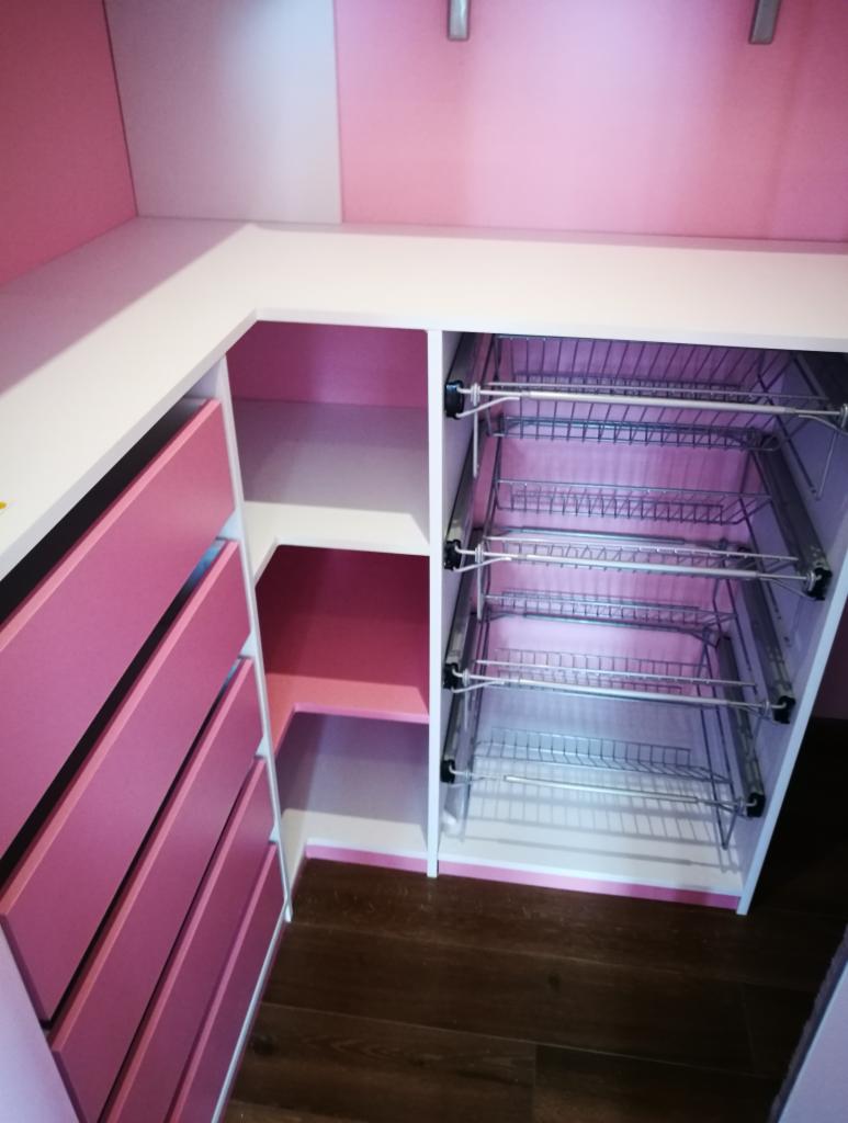 Różowo-biała zabudowa narożna z szufladami i metalowymi koszami cargo, widoczne brązowe panele podłogowe.