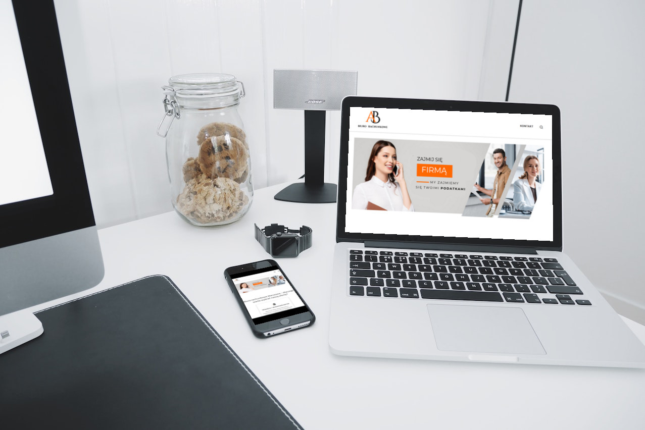Laptop i smartfon prezentują stronę internetową biura rachunkowego na białym biurku z ciasteczkami, zegarkiem i głośnikiem Bose.
