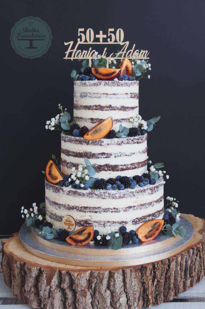 Trzypiętrowy tort 'naked cake' z owocami (tamarillo, jagody, jeżyny) i dekoracją z gipsówki, na drewnianym postumencie, z topperem '50+50 Hania i Adam'.