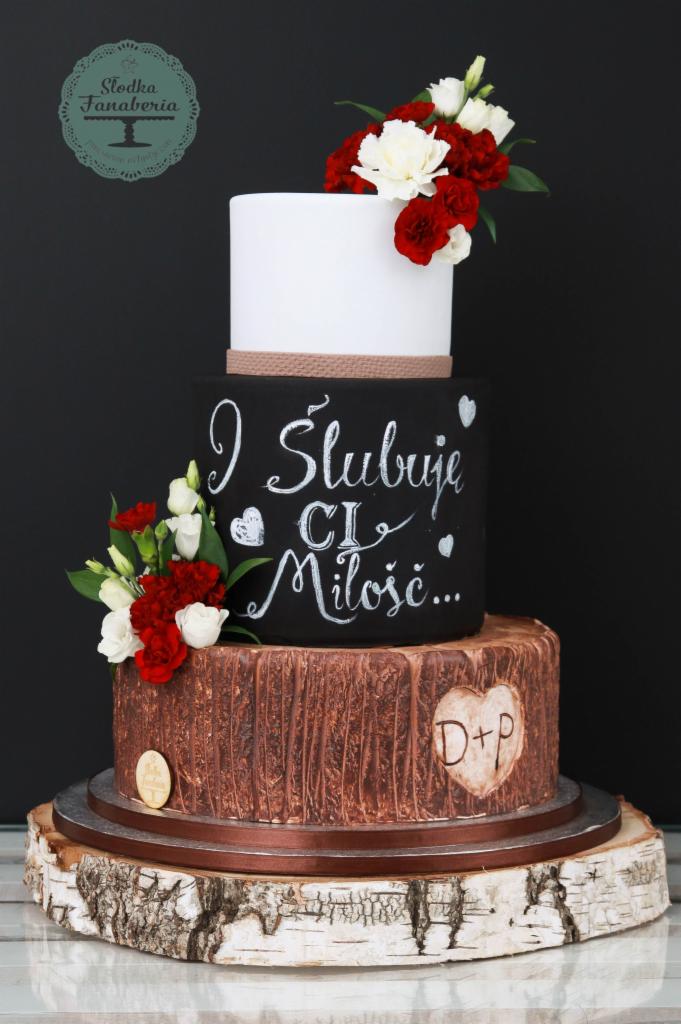 Wielopiętrowy tort weselny z motywem drewna, dekorowany kwiatami i napisem 'I Ślubuję Ci Miłość...', umieszczony na drewnianej podstawie z kory brzozy.