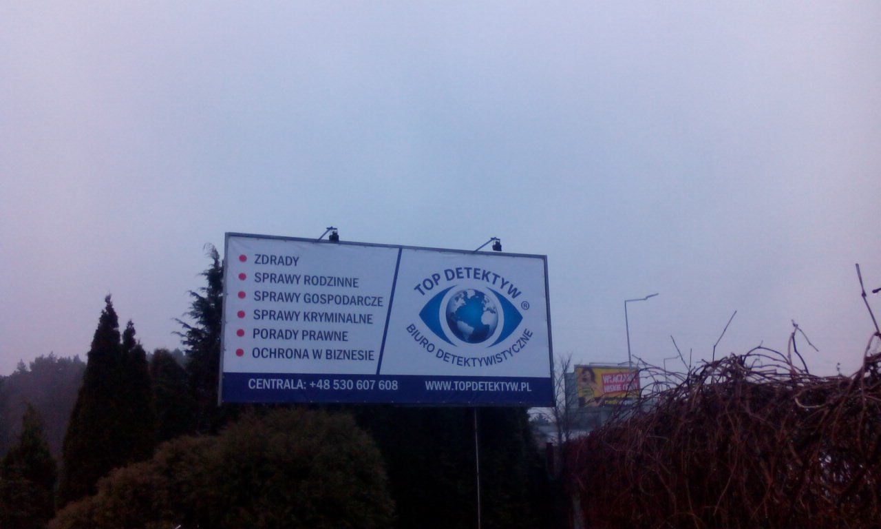 Billboard z ofertą usług biura detektywistycznego, wymieniający sprawy rodzinne, gospodarcze, kryminalne, porady prawne i ochronę w biznesie.