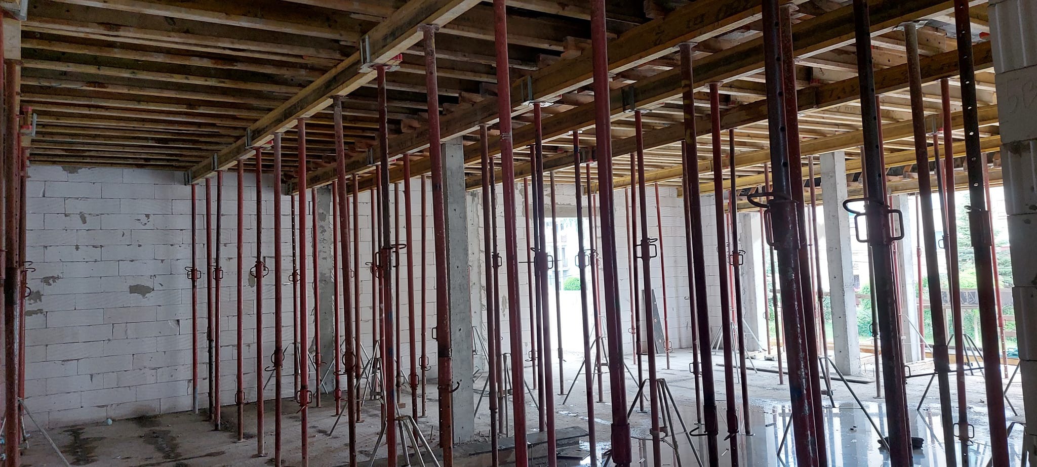 Wnętrze budynku w trakcie budowy z widocznymi podporami stropowymi, szalunkiem i ścianami z betonu komórkowego.