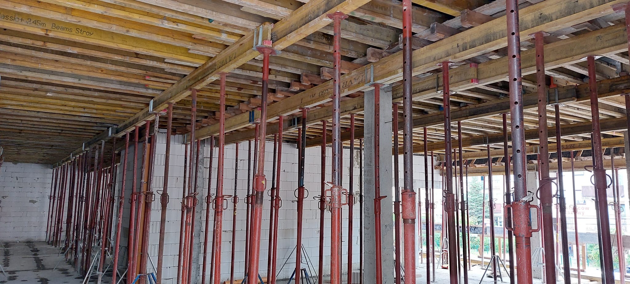 Wnętrze w trakcie budowy z widocznym szalunkiem stropu podpartym stalowymi stemplami, ściany z białego bloczka.