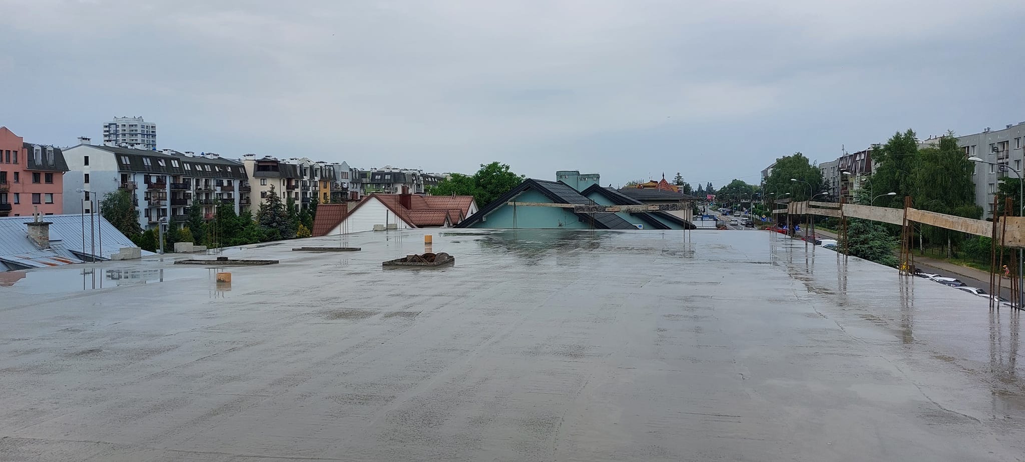 Świeżo wylana, mokra wylewka na dachu budynku wielorodzinnego, widok na miejski krajobraz w pochmurny dzień.