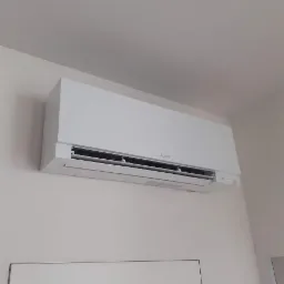 Biała jednostka klimatyzacji Mitsubishi Electric zamontowana na jasnej ścianie w pomieszczeniu, widoczne delikatne ślady po montażu na ścianie.