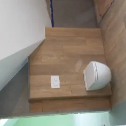 Nowoczesna toaleta podwieszana z białymi przyciskami spłukiwania zamontowana na ścianie wyłożonej płytkami imitującymi drewno, widok z góry.