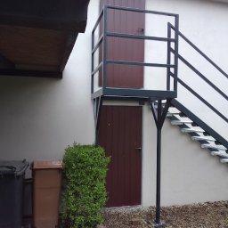 MAR-WELD Marek Stefański - Zewnętrzne schody metalowe z balustradą prowadzące do drzwi na piętrze, widoczne kosze na śmieci i mały krzew u podstawy.