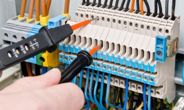 Sprawdzanie napięcia w listwie zaciskowej za pomocą wskaźnika napięcia, widoczne przewody w kolorach niebieskim i czarnym.