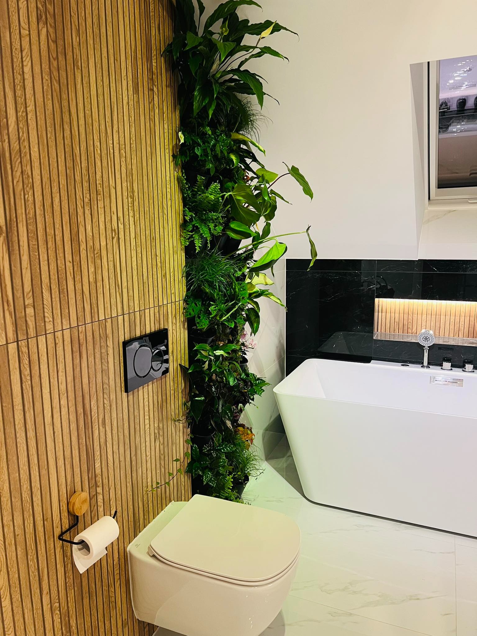 Nowoczesna łazienka z drewnianą ścianą, pionowym ogrodem, podwieszaną toaletą i wolnostojącą wanną.