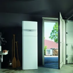 Biała pompa ciepła Vaillant w garażu z otwartymi drzwiami, widoczne wiosła, zlew i rower.