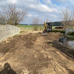 MI-KOP Usługi Ziemne Michał Kuryś - Mini koparka na działce z przygotowanym terenem pod budowę, widoczne ślady opon, ogrodzenie panelowe i shadow operatora w rogu kadru.