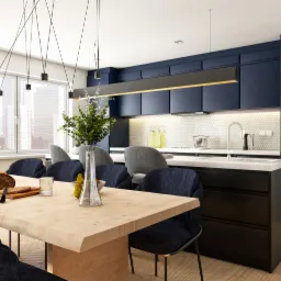 Nowoczesna kuchnia z ciemnoniebieskimi szafkami, białym blatem i heksagonalnymi płytkami na ścianie, oświetlona wiszącymi lampami nad drewnianym stołem z ciemnoniebieskimi krzesłami i dekoracjami.