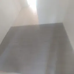 Szara podłoga z paneli ułożona w jasnym pomieszczeniu z białymi ścianami. Widok z góry, ukośne ujęcie.