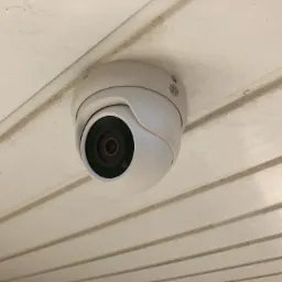 Kamera kopułkowa monitoringu zamontowana na białym, panelowym suficie z widocznymi drobnymi zabrudzeniami wzdłuż łączeń paneli.