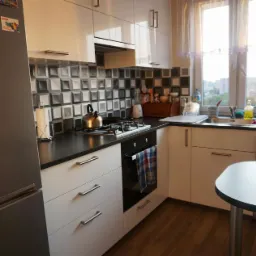 Nowoczesna kuchnia z białymi szafkami, czarnym blatem i mozaiką na ścianie, widok na miasto przez okno, z logo firmy w prawym dolnym rogu.