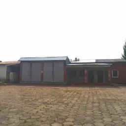 Budynek gospodarczy z cegły, z zasłoniętymi wjazdami, widok z zewnątrz na plac wyłożony kostką brukową.