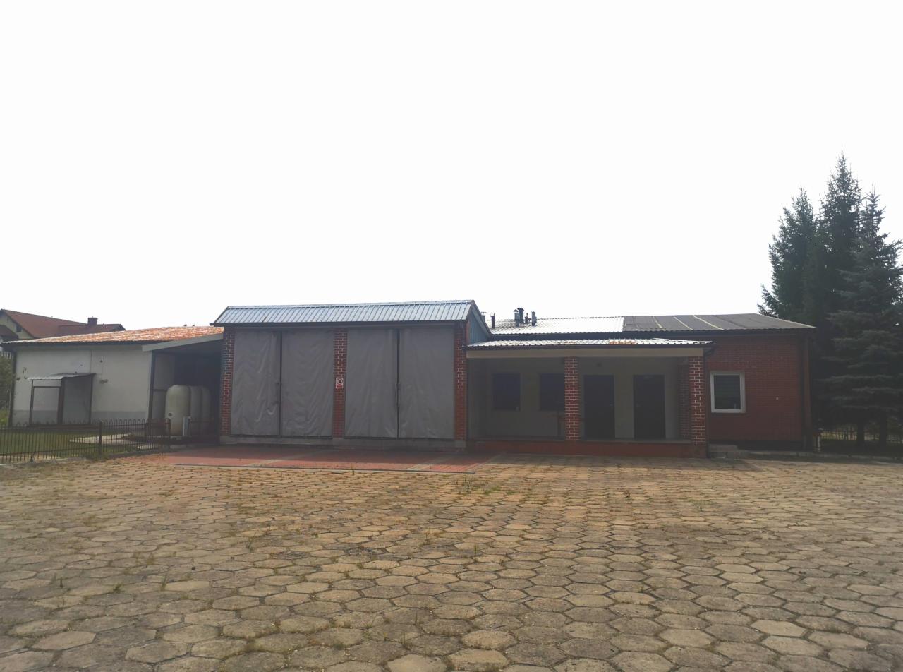 Budynek gospodarczy z cegły, z zasłoniętymi wjazdami, widok z zewnątrz na plac wyłożony kostką brukową.