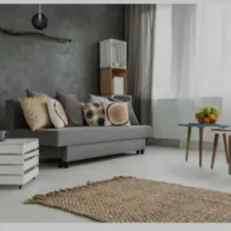 Szary salon z teksturowaną ścianą, szarą sofą z dekoracyjnymi poduszkami, białym stolikiem z drewnianych skrzynek, dywanem z juty i zestawem stolików kawowych.