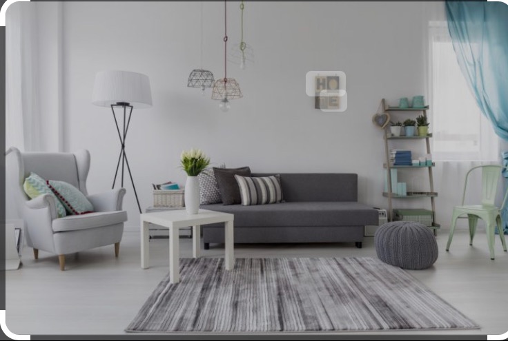 Jasne, przestronne wnętrze salonu z szarą sofą, wzorzystym dywanem, białym stolikiem i krzesłem w odcieniu mięty.