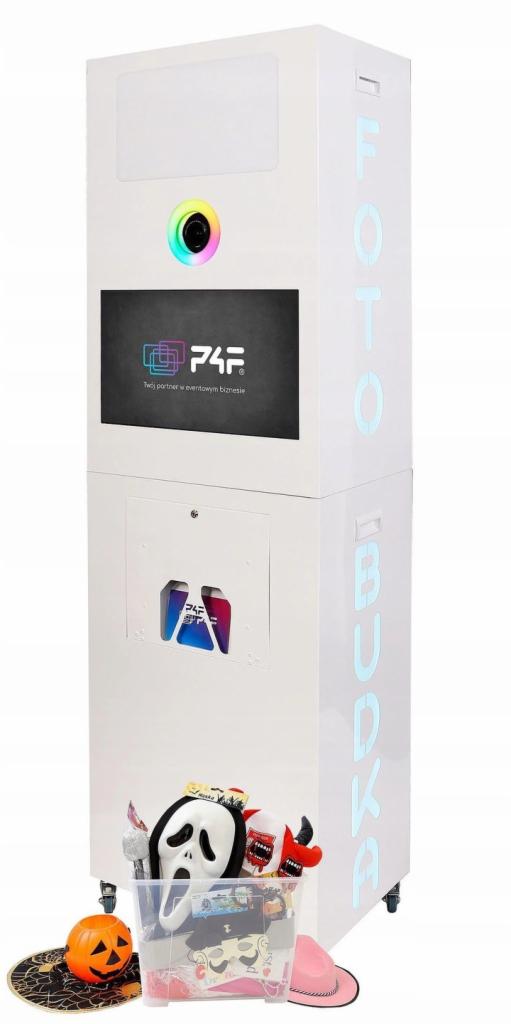 Biała fotobudka z neonowym napisem 'FOTOBUDKA' z boku, ekranem dotykowym, tęczową obwódką wokół obiektywu kamery i przezroczystym pojemnikiem z rekwizytami do zdjęć, takimi jak maski i kapelusze...