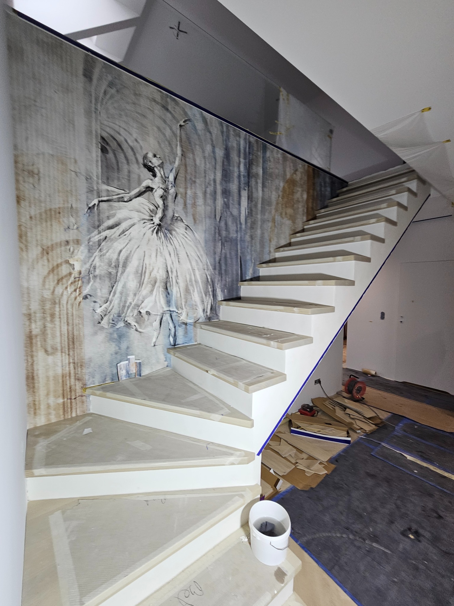 Ściana z fototapetą przedstawiającą baletnicę w pokoju ze schodami w trakcie wykończenia, widoczne narzędzia i materiały budowlane.