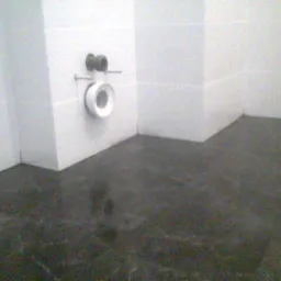 Świeżo położona, ciemna, błyszcząca posadzka w łazience z białymi, błyszczącymi płytkami na ścianach i wystającym przyłączem kanalizacyjnym.