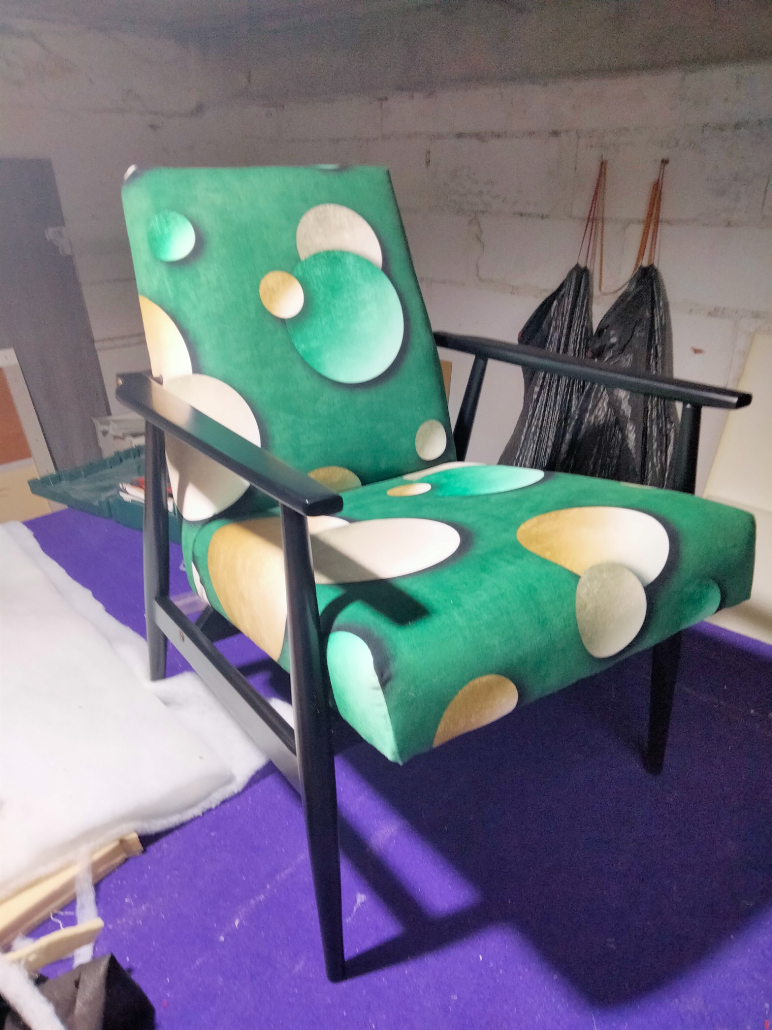 Odrestaurowany fotel z lat 60. w Szczecinie, z nową, zieloną tapicerką w geometryczne wzory, czarne drewniane nóżki i podłokietniki, na tle warsztatu.