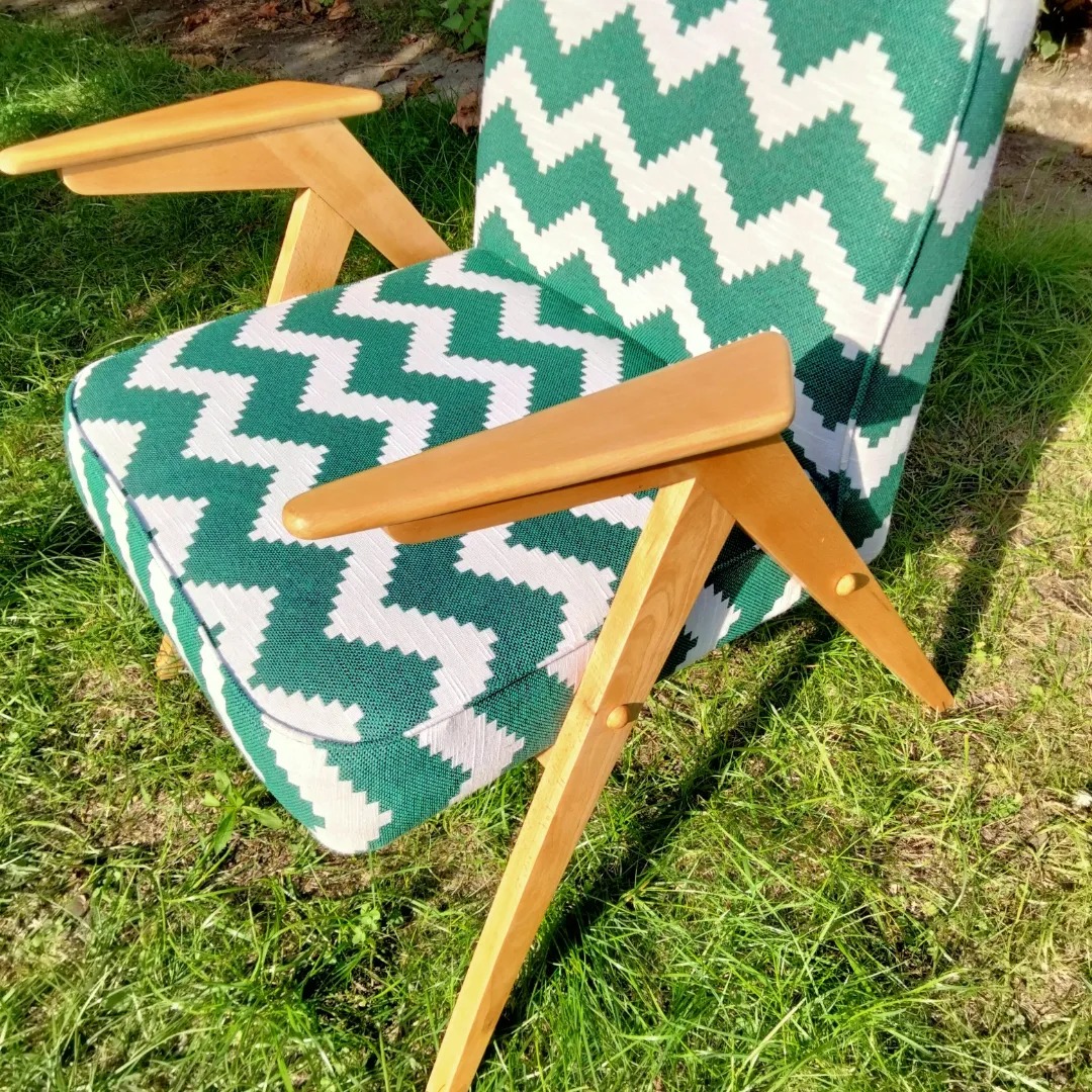 Fotel z drewnianymi podłokietnikami i zielono-białym zygzakowatym wzorem tapicerki, ustawiony na trawie w słoneczny dzień.