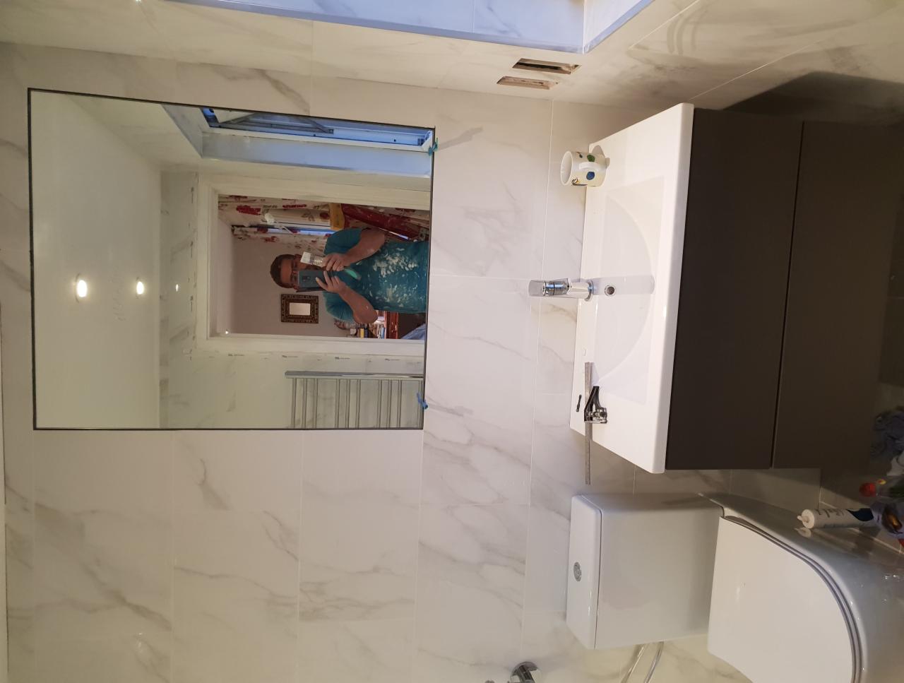 Ukończona łazienka z marmurowymi płytkami, wiszącą szafką z umywalką i toaletą. W lustrze odbija się osoba robiąca zdjęcie.