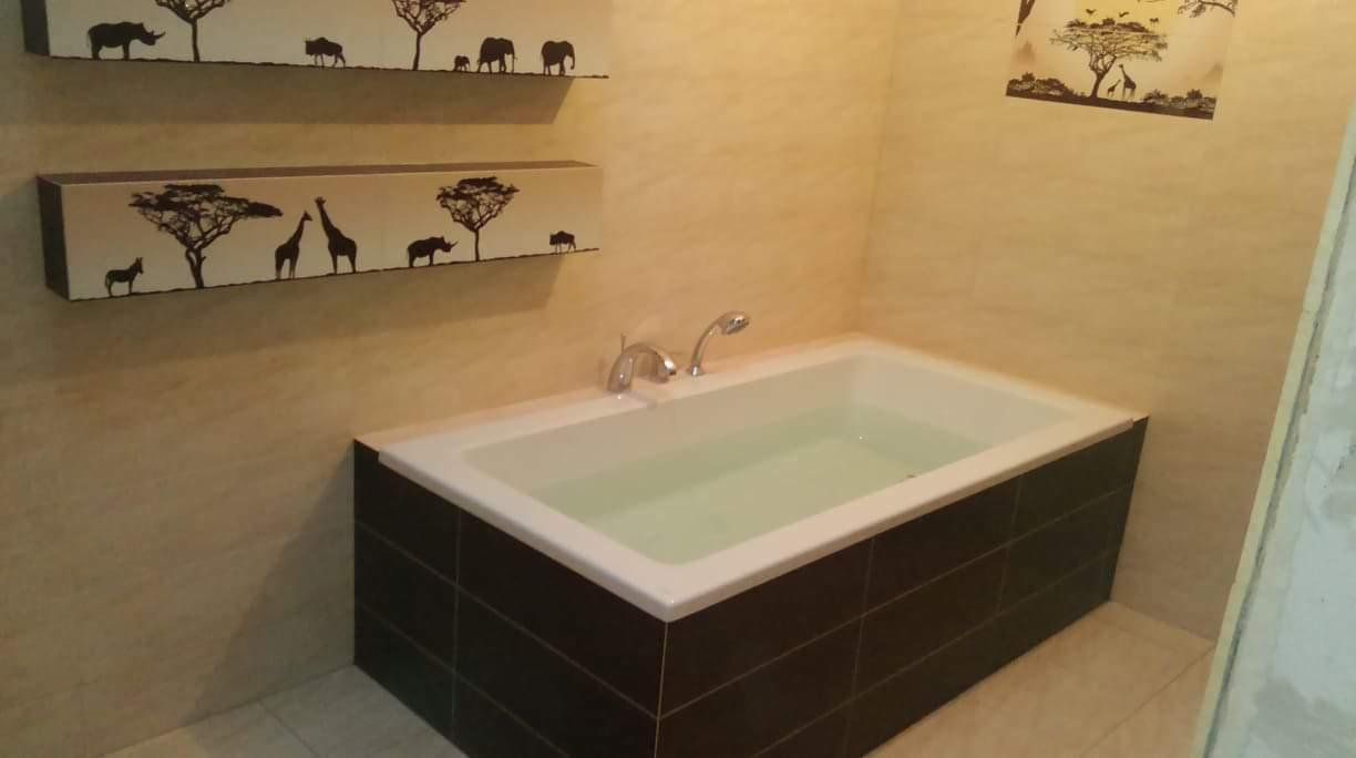 Wanna z ciemną obudową z płytek, wypełniona wodą, na ścianach półki i naklejki z motywami afrykańskimi.