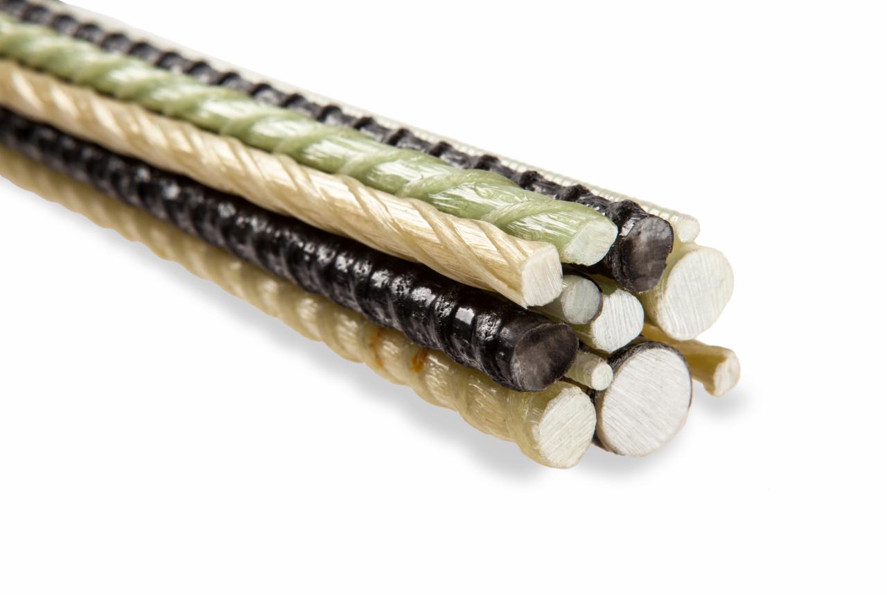 Kompozytowe pręty zbrojeniowe w kolorach czarnym, beżowym i zielonym, ułożone w stos na białym tle, widoczne przekroje poprzeczne o różnych średnicach.