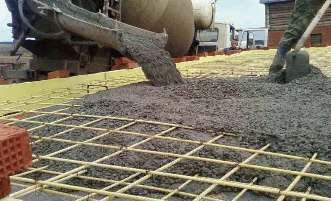 Wylewanie betonu na żółtą siatkę zbrojeniową, widoczny mikser do betonu i pracownik z łopatą.