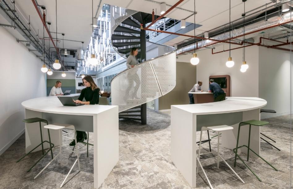 Wnętrze biurowe z otwartą przestrzenią, spiralnymi schodami i widocznymi instalacjami elektrycznymi pod sufitem.