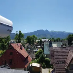 Kamera monitoringu IP marki POV zamontowana na zewnątrz budynku, z widokiem na panoramę miasta i góry w tle.