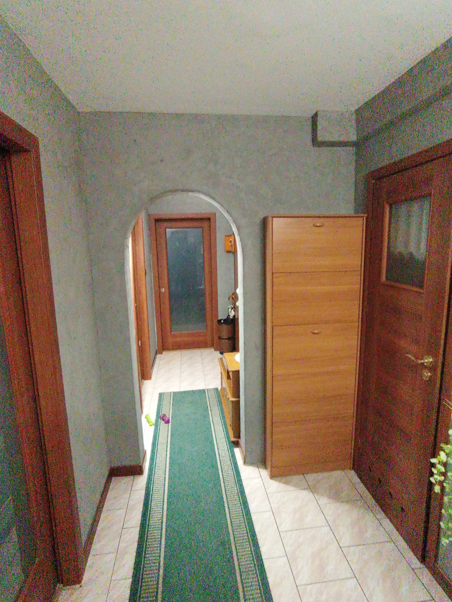 Korytarz po odświeżeniu: szare ściany z delikatną fakturą, drewniane drzwi i szafka na buty, zielony dywanik w pasy.