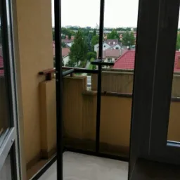 Metalowa konstrukcja na balkonie z widokiem na osiedle domów jednorodzinnych, zabezpieczona folią malarską.