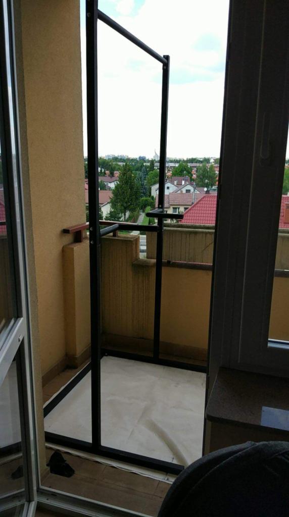 Metalowa konstrukcja na balkonie z widokiem na osiedle domów jednorodzinnych, zabezpieczona folią malarską.