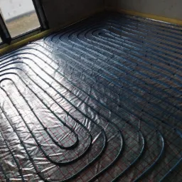 Układanie rur ogrzewania podłogowego na folii izolacyjnej z siatką w Ramiszowie, widok z góry, surowy stan wykończenia.