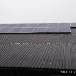 Panele słoneczne na blaszanym dachu w Czarnej, widoczne z dołu pod kątem, pochmurne niebo.