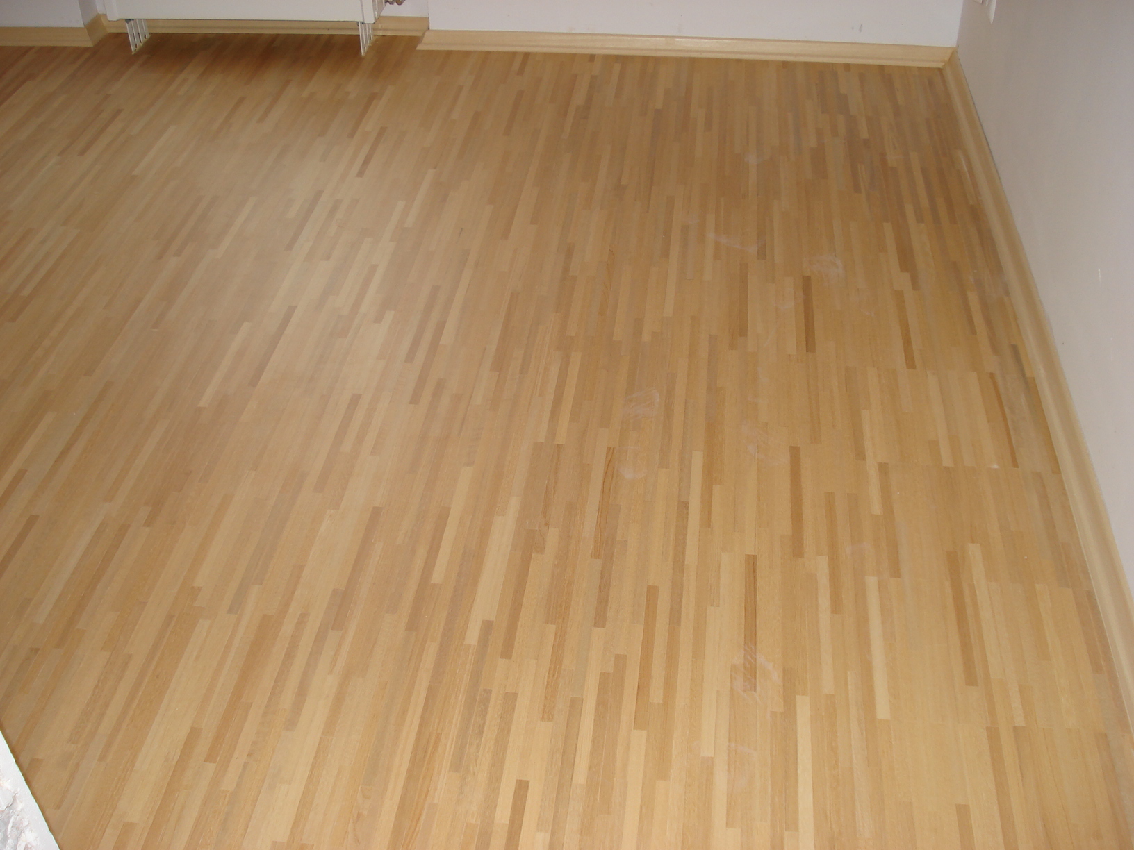 Jasny, nowo ułożony parkiet w pomieszczeniu z białymi ścianami i listwami przypodłogowymi.