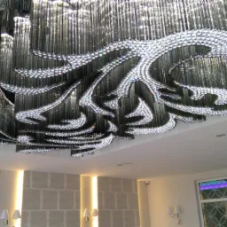 Imponujący żyrandol sufitowy z elementami kryształowymi i szklanymi rurkami, oświetlający wnętrze z dekoracyjnymi panelami ściennymi i oknami z wzorami.