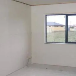 Surowe ściany w pokoju z oknem, przygotowane do dalszych prac wykończeniowych. Widoczne łączenia płyt kartonowo-gipsowych przed szpachlowaniem.