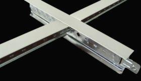 Metalowy profil konstrukcyjny w kształcie litery T, prawdopodobnie do sufitu podwieszanego, widoczny z bliska na czarnym tle.